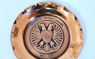 1967_plat_societe_chorale_orpheon_mhl Plat circulaire en cuivre avec pourtour martelé. Au centre, il porte en bas-relief l'emblème de l'Orphéon, entouré d'un aigle bicéphale, 1967.